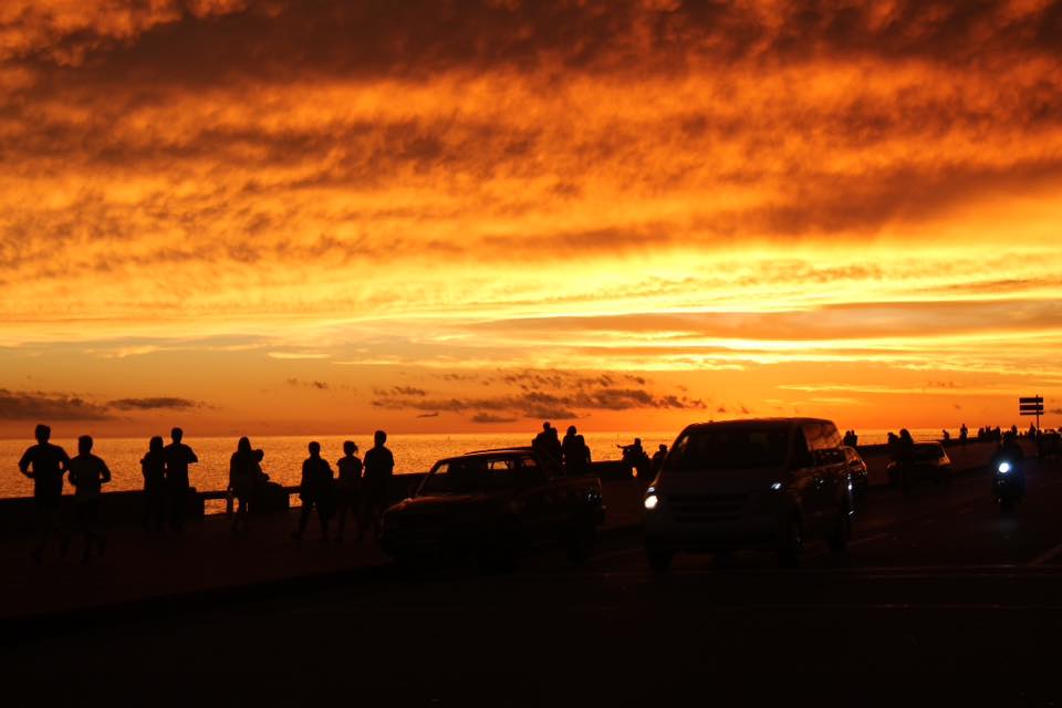 An orange sunset over the sea with silhouettes along the waterfront.